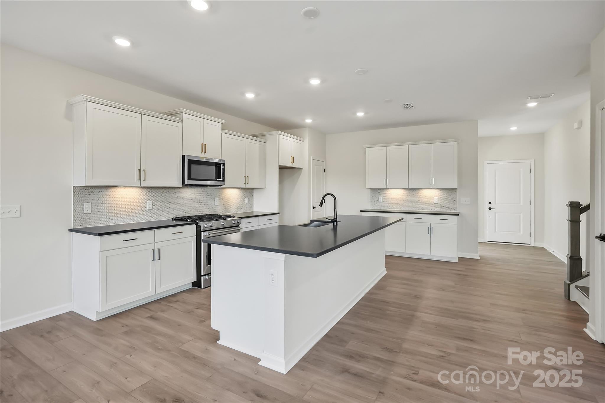 1821 Riverbend Avenue, Unit 85 Monroe, NC 28110 - Photo 5 of 15 a large kitchen with stainless steel appliances kitchen island granite countertop a stove a sink a refrigerator and white cabinets with wooden floor