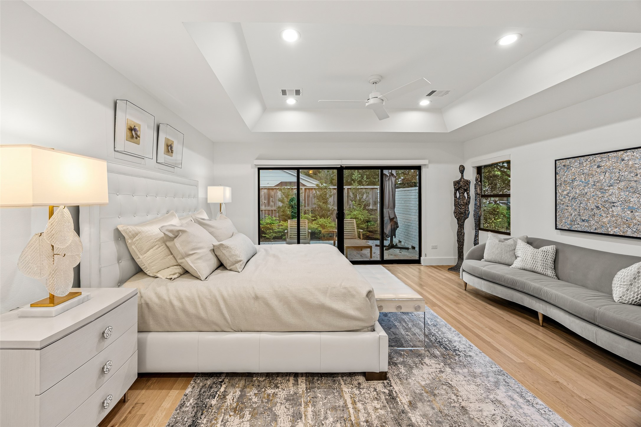 5658 Del Monte Drive Houston, TX 77056 - Photo 13 of 35 Step into a primary suite designed as a true private retreat—where modern elegance meets calming comfort. This spacious bedroom features a dramatic tray ceiling with recessed lighting, creating a soft, inviting glow throughout the room. Wide-plank hardwood floors add warmth and sophistication, while an oversized slider seamlessly opens to the backyard, offering a serene indoor-outdoor connection perfect for morning coffee or evening unwinding.