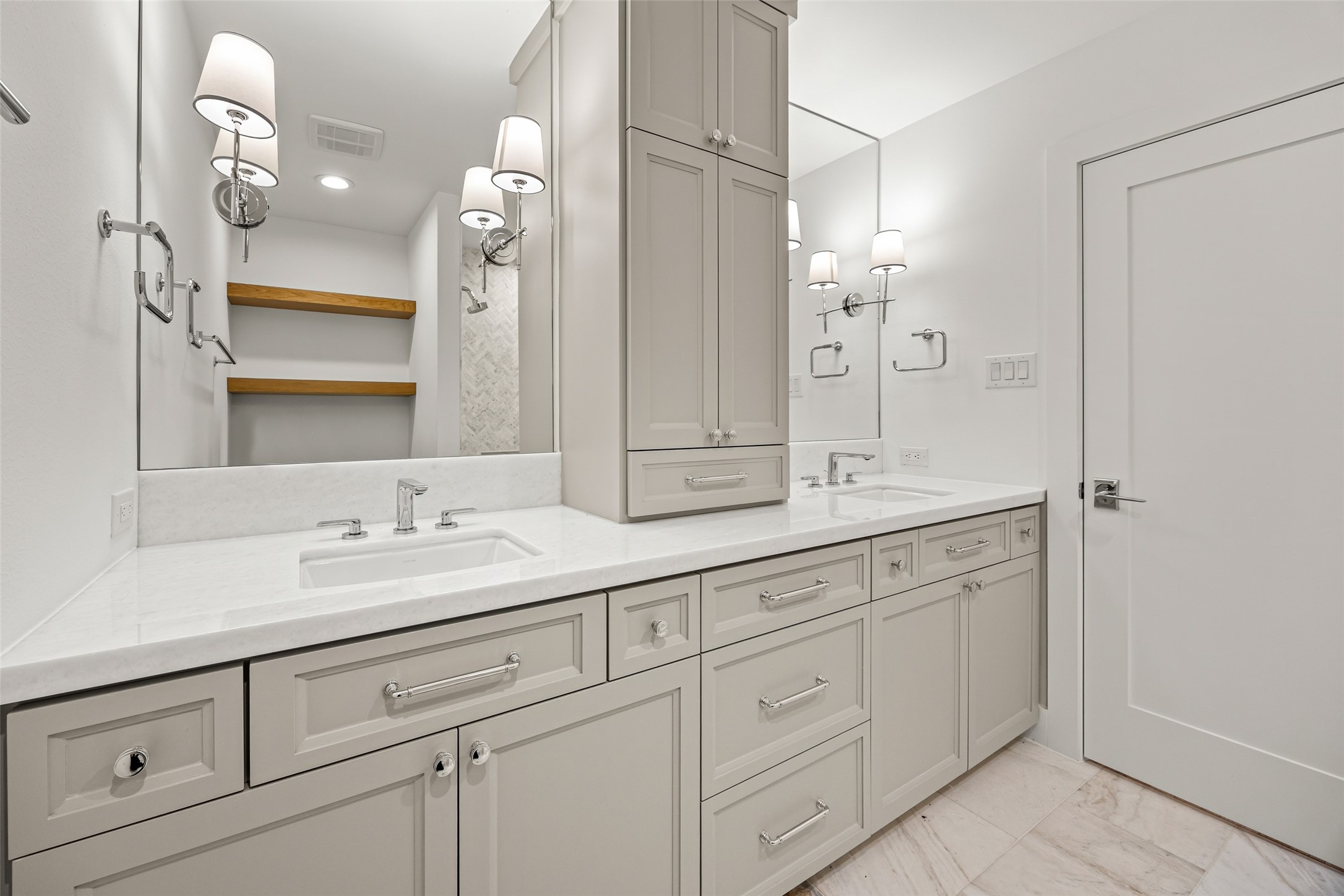 5658 Del Monte Drive Houston, TX 77056 - Photo 16 of 35 The double vanity features custom cabinetry, slab countertops, elegant sconce lighting, and abundant storage—including a central tower for everyday convenience. The suite continues into an expansive, fully built-out walk-in closet with adjustable shelving, drawers, and generous hanging space, designed to accommodate even the most extensive wardrobe.
This entire wing of the home feels like stepping into a modern boutique hotel—private, calming, and beautifully executed.