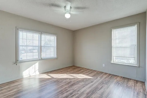 an empty room with wooden floor ceiling fan and windows