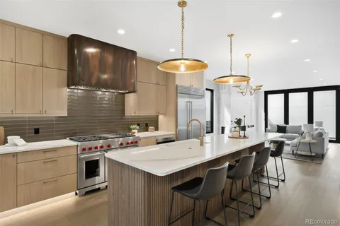 a kitchen with a stove a kitchen island a sink white cabinets and couches with wooden floor