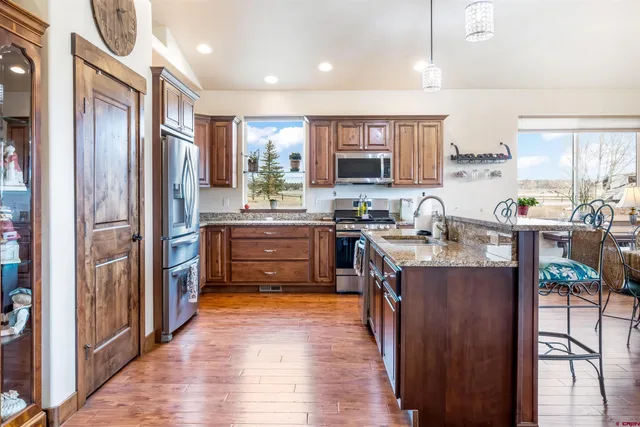 a kitchen with stainless steel appliances granite countertop a refrigerator a sink dishwasher a stove and a dining table with wooden floor