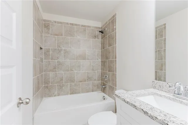 a bathroom with a granite countertop bathtub shower sink vanity and toilet