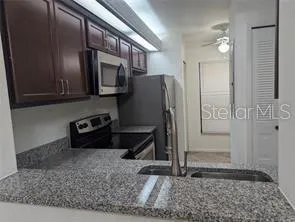 a kitchen with stainless steel appliances granite countertop a refrigerator a stove and a sink with wooden cabinets