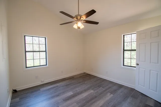 an empty room with wooden floor fan and windows