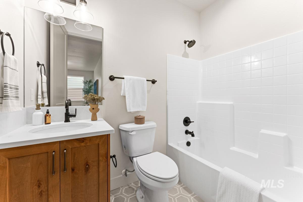 13338 North Spring Creek Way Boise, ID 83714 - Photo 26 of 46 Bathroom featuring a wood-finish vanity with a white countertop and integrated sink, a rectangular mirror, and a full bathtub with white subway tile surround