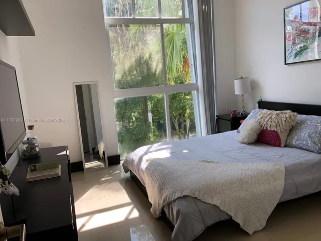 a bedroom with a bed a flat tv screen and a large window