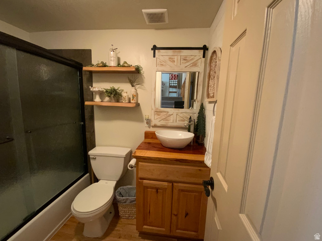 1061 Copper Street Stockton, UT 84071 - Photo 20 of 43 Bathroom featuring a shower-tub combination with sliding glass doors, a toilet, a wood vanity with a white vessel sink, a coordinating wood-framed mirror, and two floating wood shelves
