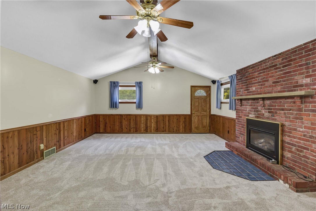 301 Crosse Road Amherst, OH 44001 - Photo 16 of 49 Spacious room featuring vaulted ceilings with dual ceiling fans, a red brick fireplace with a wood mantel, and light-toned carpet flooring