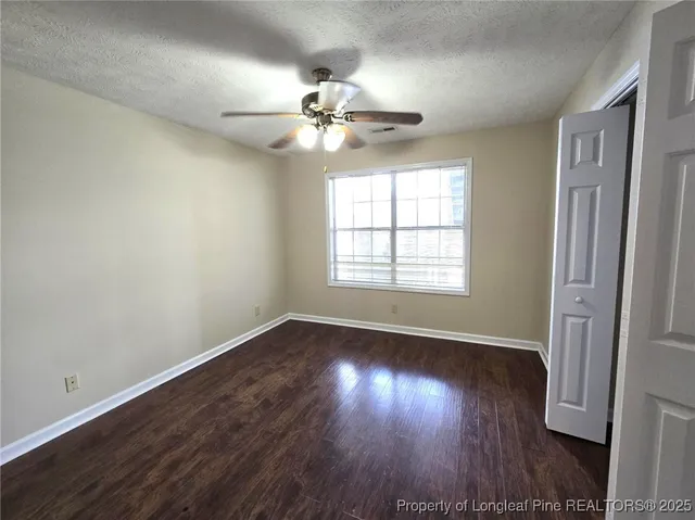an empty room with wooden floor chandelier fan and windows
