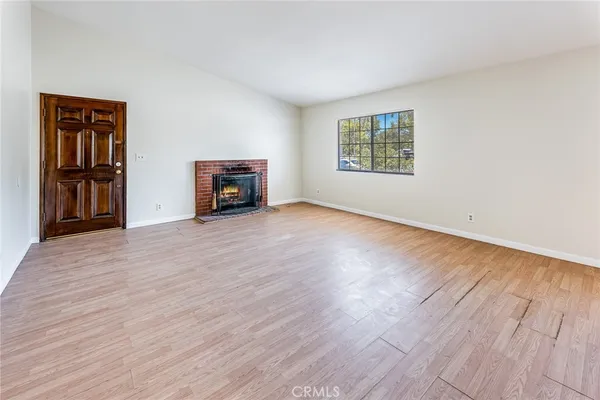 an empty room with wooden floor fireplace and windows