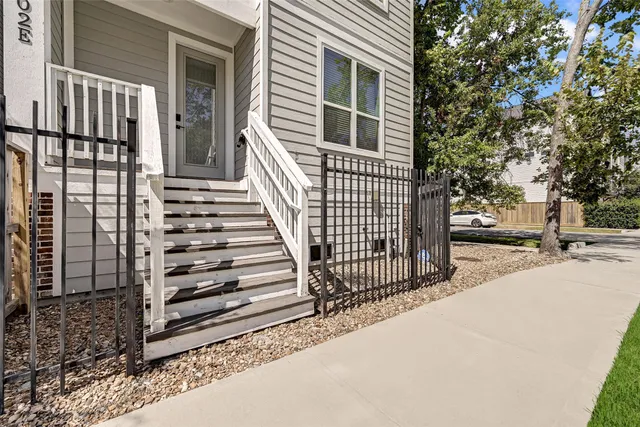 a view of a brick house with wooden fence and large trees
