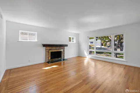 a view of a big room with wooden floor fire place and windows