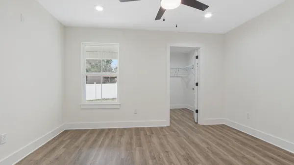 an empty room with wooden floor chandelier fan and windows