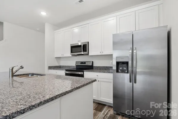 a kitchen with granite countertop a refrigerator a sink a stove and cabinets