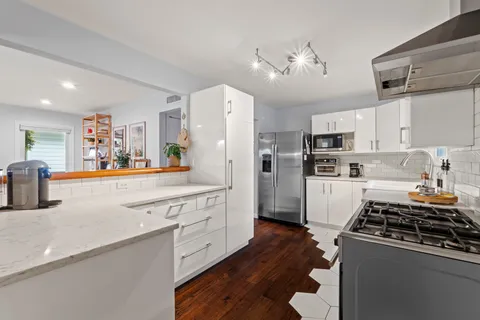 a kitchen with stainless steel appliances granite countertop a refrigerator a sink dishwasher a stove and white cabinets with wooden floor