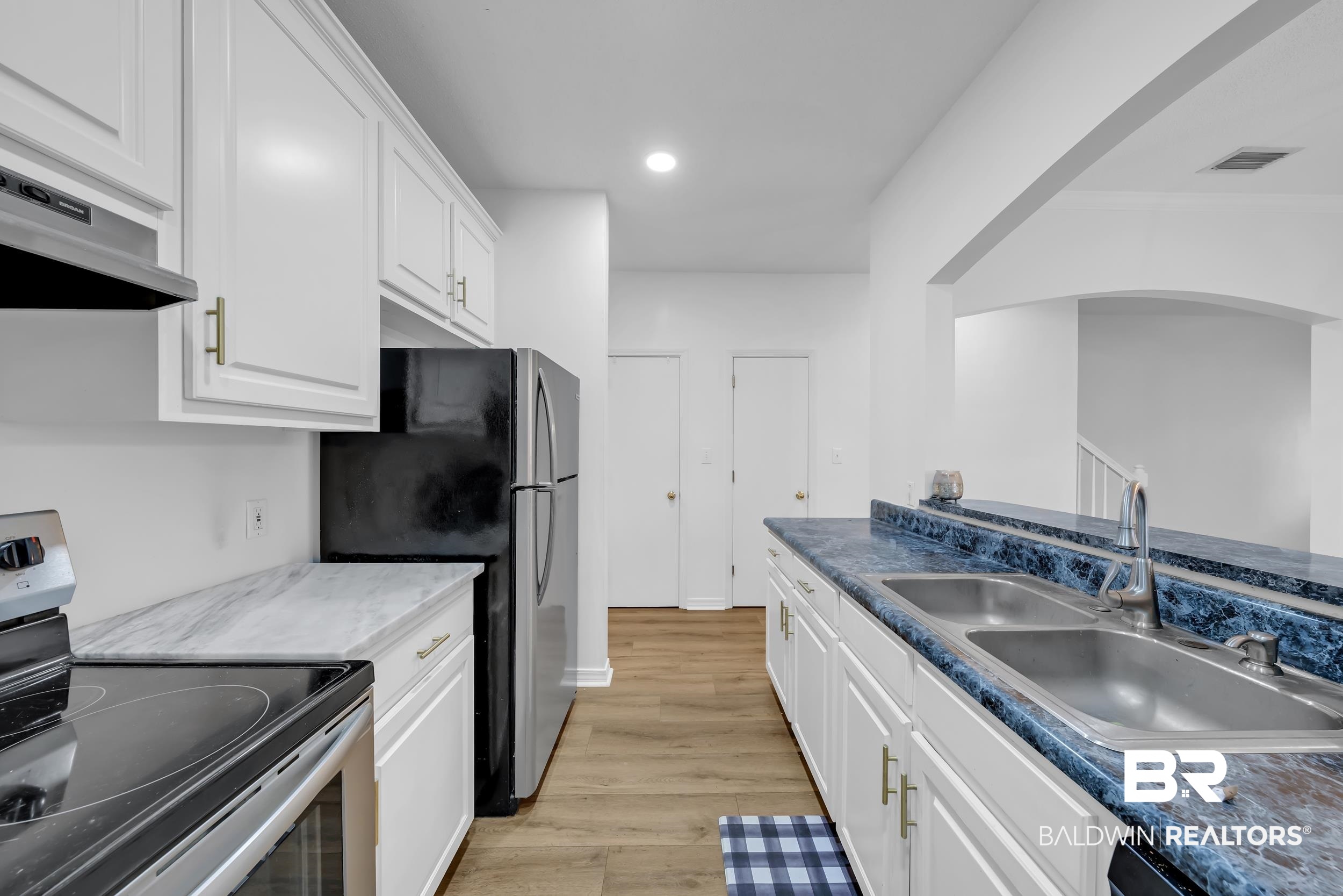 17488 Pandion Ridge, Unit A1 Fairhope, AL 36532 - Photo 9 of 18 Kitchen featuring white cabinetry with gold-finish hardware, a stainless steel double basin sink, and wood-finish flooring