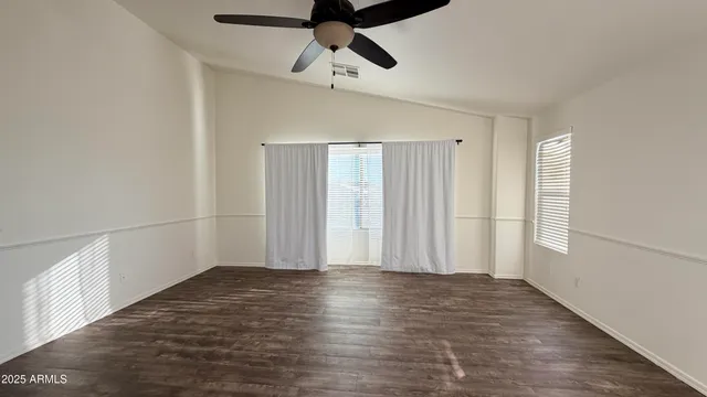 an empty room with wooden floor fan and windows