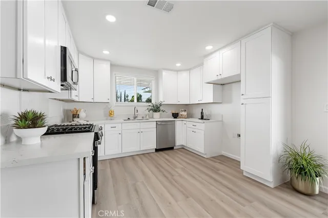 a kitchen with white cabinets white appliances sink and a potted plant