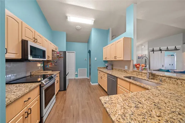 a open kitchen with stainless steel appliances granite countertop a stove top oven a sink dishwasher and a microwave oven with large wooden cabinets