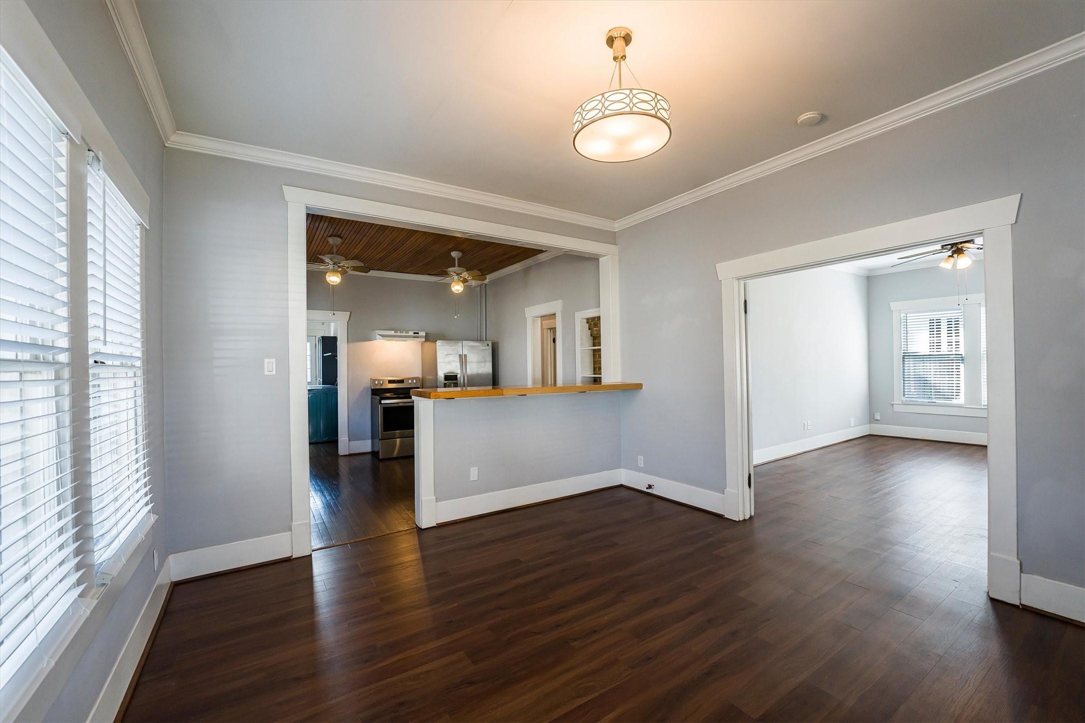 210 Tabor Street Houston, TX 77009 - Photo 5 of 18 This photo showcases a bright, open-concept living space with hardwood floors and neutral walls. The area features a modern light fixture, large windows with blinds, and a pass-through to the kitchen, which includes stainless steel appliances. A separate room is visible, ideal for a dining or living area.