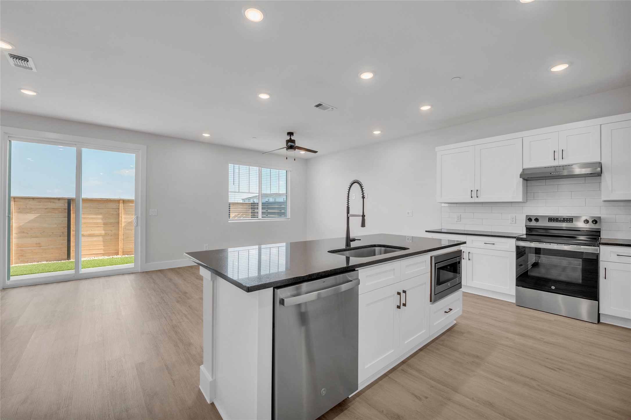 9317 Curious Squirrel Street Austin, TX 78744 - Photo 3 of 26 Kitchen with stainless steel appliances, white cabinets, ceiling fan, light wood finished floors, and a kitchen island with sink