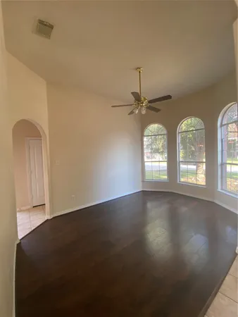 an empty room with wooden floor fan and windows