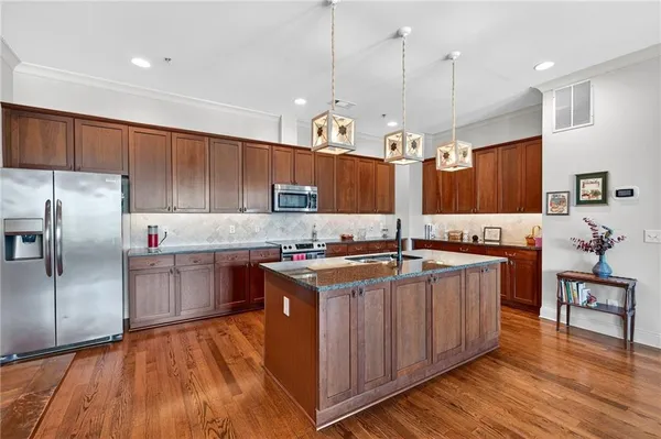 a kitchen with stainless steel appliances granite countertop wooden floors wooden cabinets a center island and a window