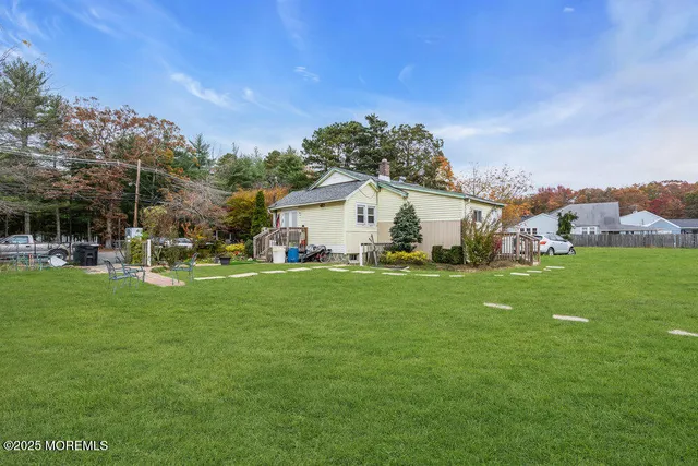 a view of a white house in front of a big yard with plants and large trees