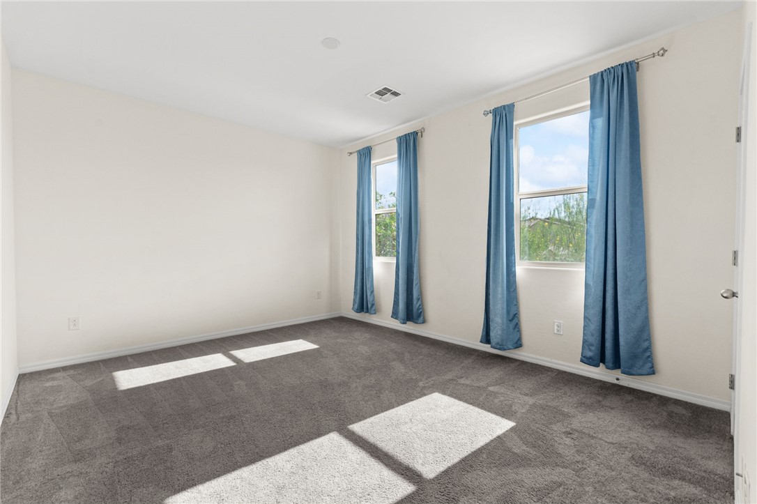 11048 Prairie Grove Road Las Vegas, NV 89179 - Photo 56 of 75 Two windows with light blue curtains allow natural light to fill this carpeted bedroom, offering a serene escape.