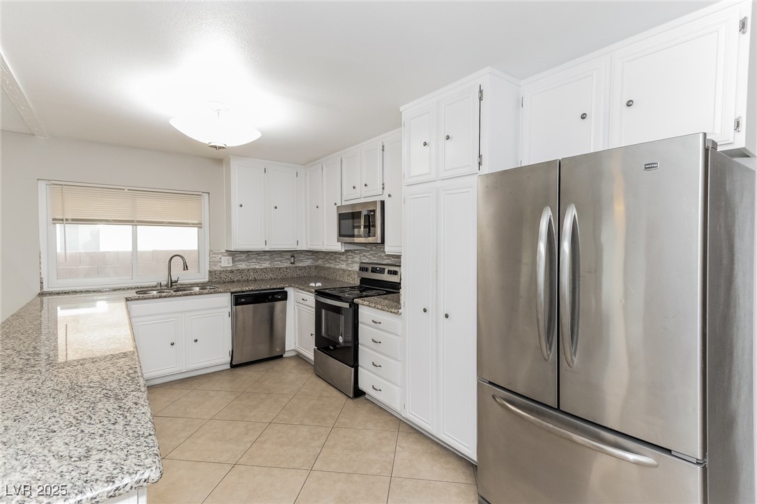 4737 Monaco Road Las Vegas, NV 89121 - Photo 12 of 21 Kitchen featuring stainless steel appliances, light stone countertops, light tile patterned flooring, backsplash, and white cabinetry