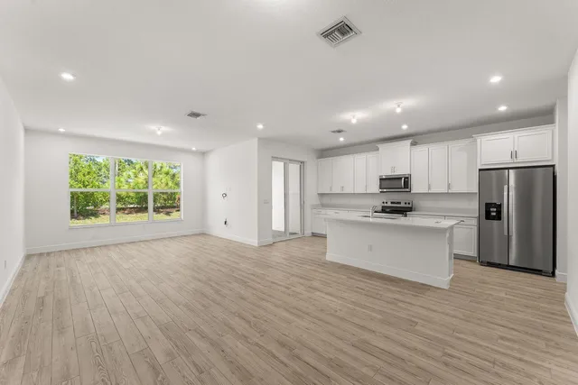 a large white kitchen with stainless steel appliances granite countertop a stove a refrigerator a sink and a large window with wooden floor