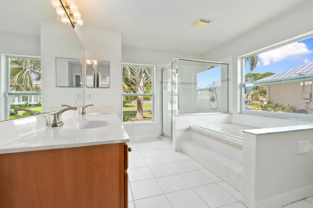 a spacious bathroom with stainless steel appliances granite countertop a sink a bathtub a mirror and next to a window
