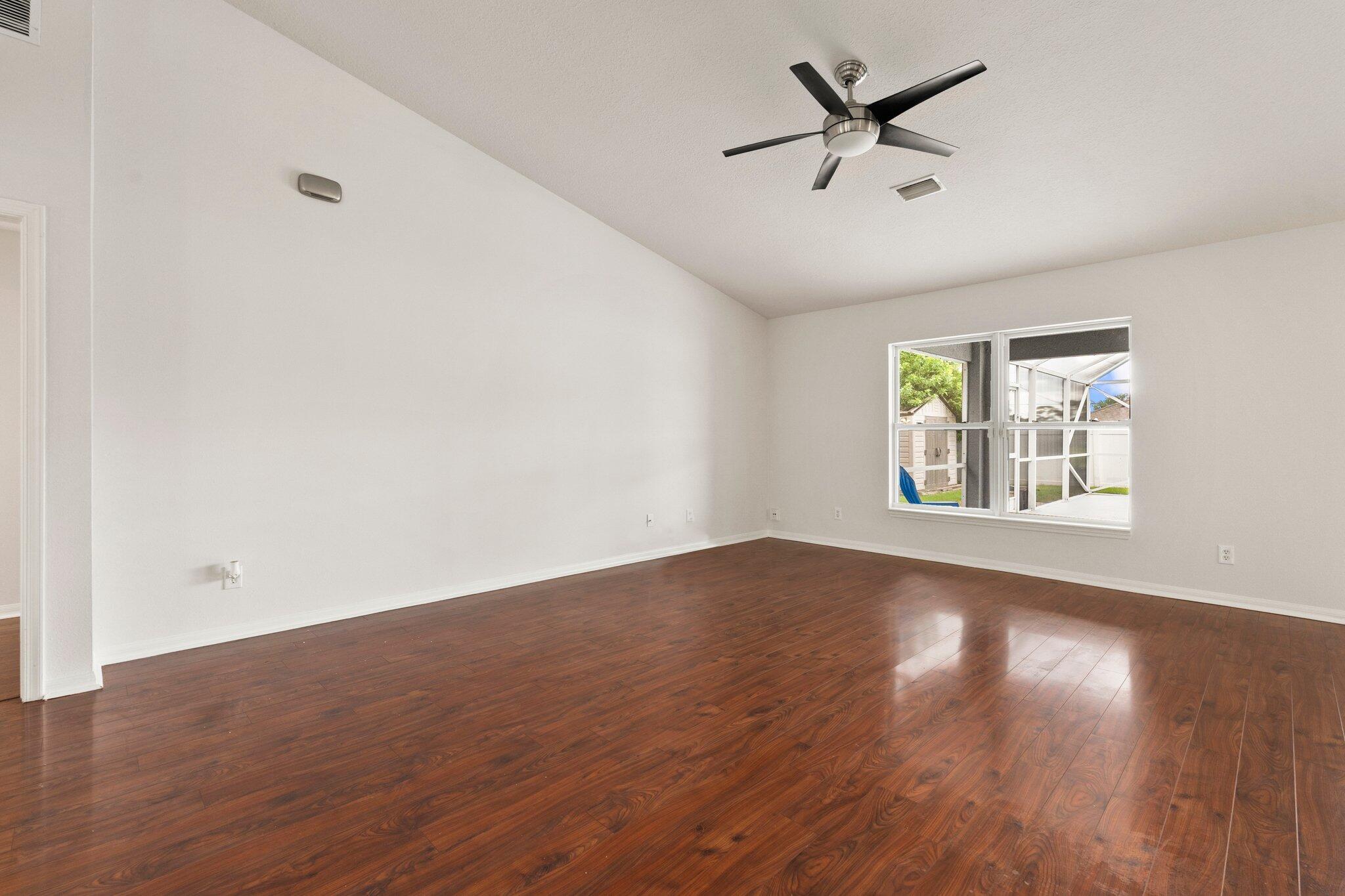 1901 Southwest Diamond Street Port St. Lucie, FL 34953 - Photo 9 of 42 an empty room with wooden floor chandelier fan and windows
