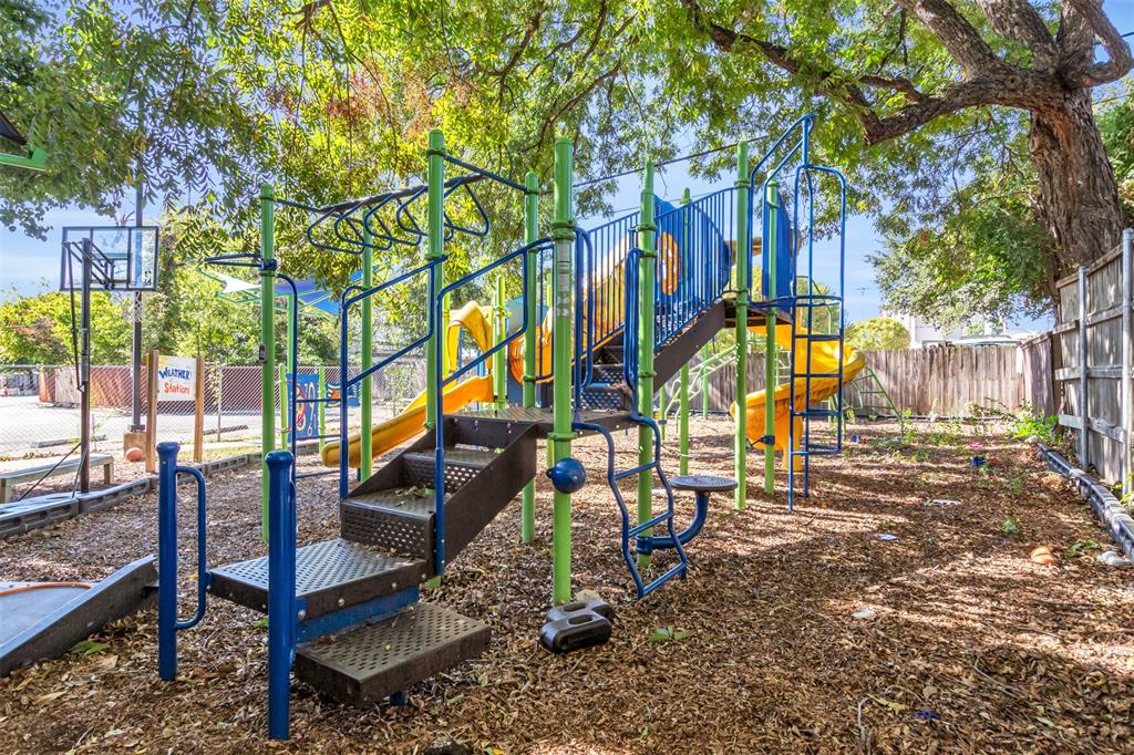 4121 Junius Street, Unit B Dallas, TX 75246 - Photo 5 of 32 Outdoor play area featuring a multi-level play structure with slides and monkey bars, basketball hoop, and wood chip ground cover, all shaded by mature trees