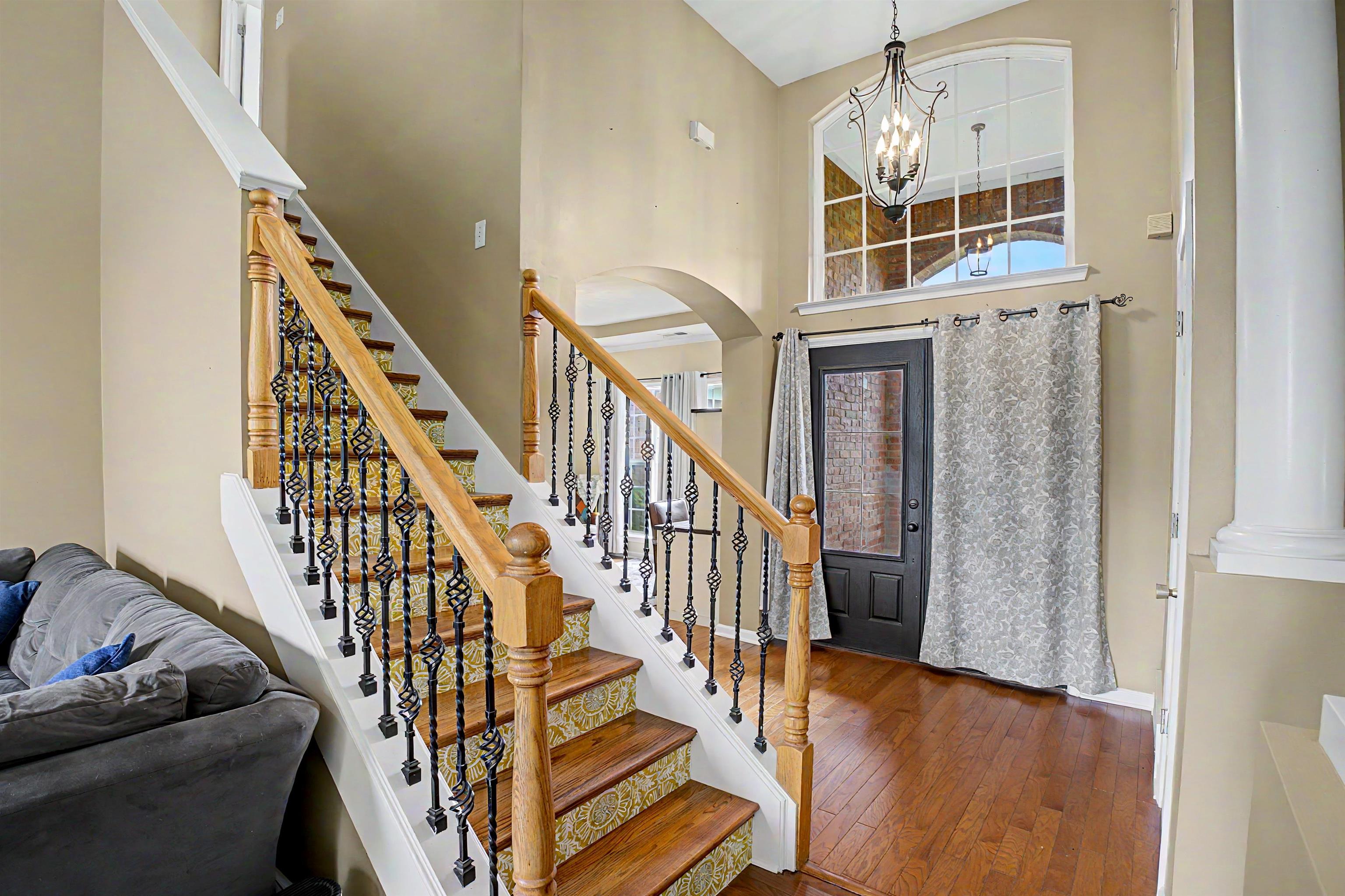 134 Rembert Drive Atoka, TN 38004 - Photo 6 of 38 Grand foyer featuring hardwood flooring, a prominent staircase with decorative iron balusters and wood handrails, a black door with frosted glass, and an arched transom window