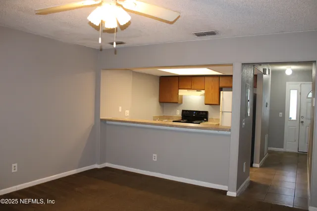 an empty room with a chandelier fan and wooden floor
