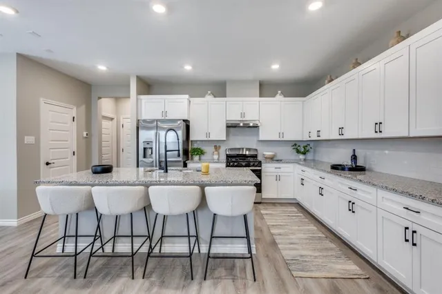 a kitchen with stainless steel appliances kitchen island granite countertop a table chairs sink and cabinets