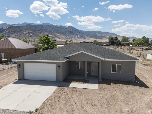 51 West 500 South Monroe, UT 84754 - Photo 30 of 41 Single-story residence featuring a gray stucco exterior, dark shingle roof, and a prominent two-car garage with a white door