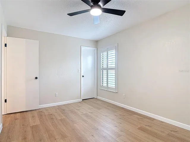 an empty room with wooden floor fan and windows