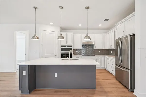 a large kitchen with kitchen island a stove a sink a refrigerator and a wooden floor