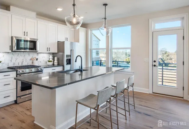 a kitchen with stainless steel appliances granite countertop a stove a sink a microwave refrigerator and chairs