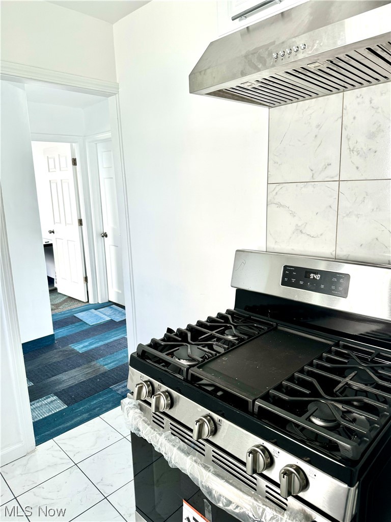 Kitchen with wall chimney exhaust hood, light tile floors, and stainless steel gas range