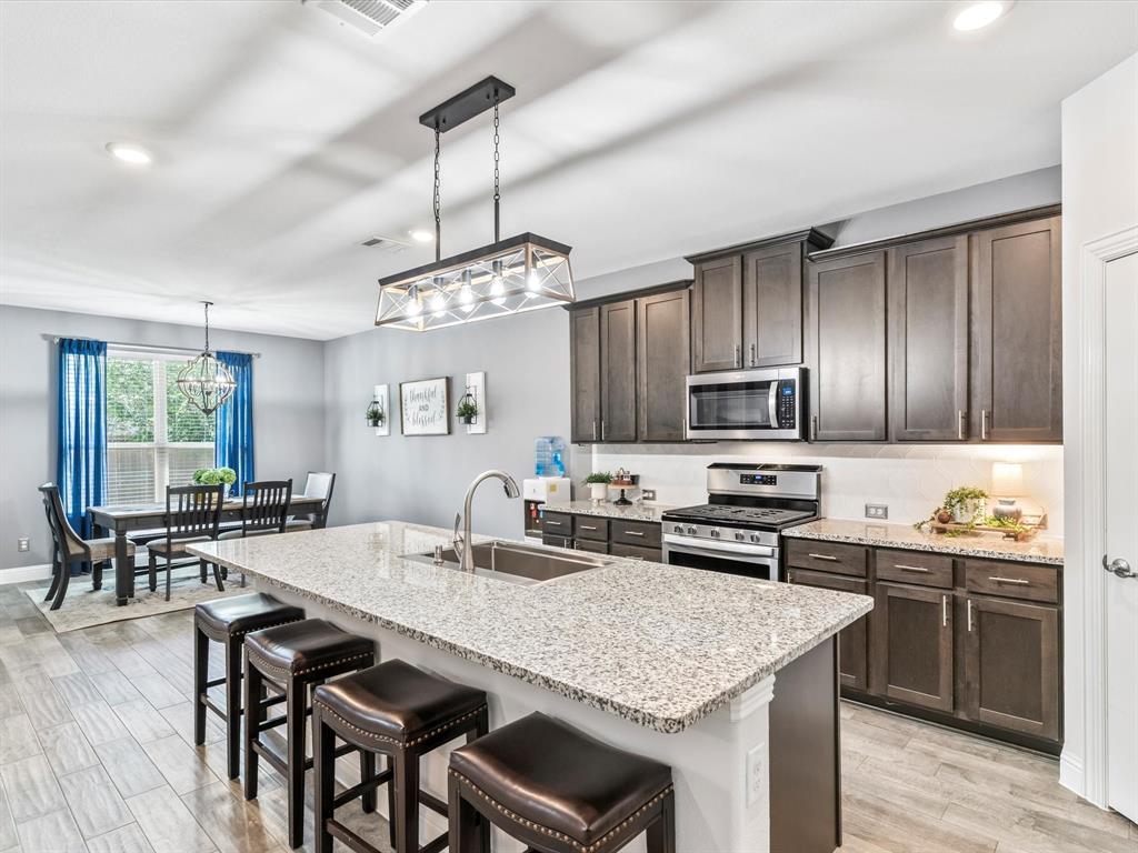 a kitchen with stainless steel appliances granite countertop a stove top oven a sink a dining table and chairs with wooden floor