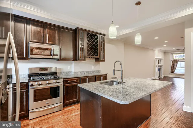 a kitchen with stainless steel appliances granite countertop a kitchen island a stove a sink dishwasher and microwave with wooden floor