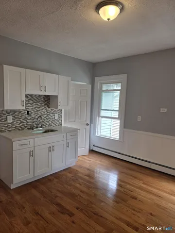 a kitchen with granite countertop a stove a sink and white cabinets with wooden floor