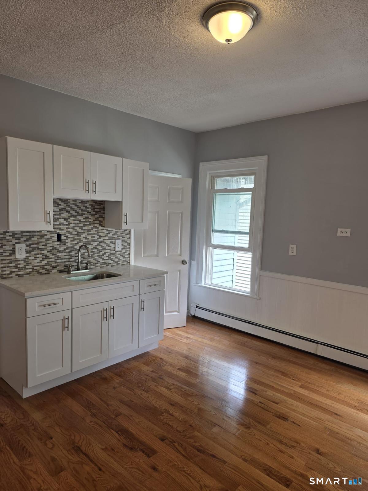 a kitchen with granite countertop a stove a sink and white cabinets with wooden floor