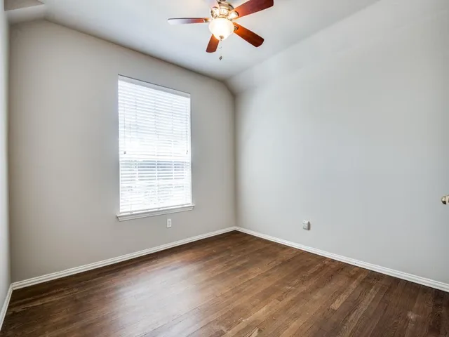 an empty room with wooden floor ceiling fan and windows