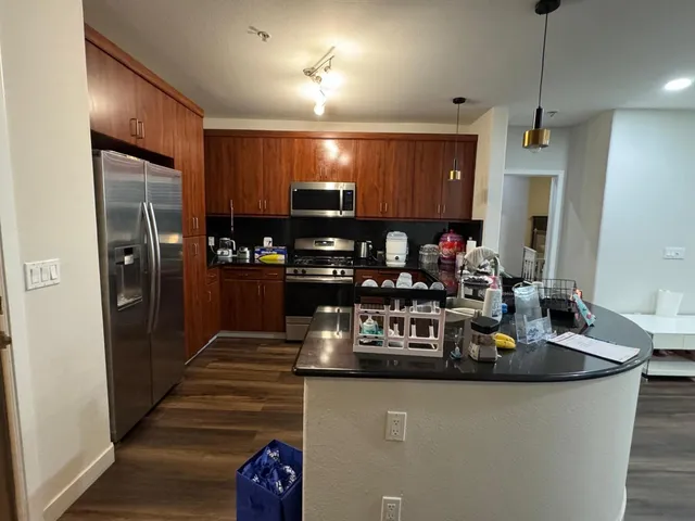 a kitchen with kitchen island granite countertop a refrigerator a stove and a sink with wooden floor