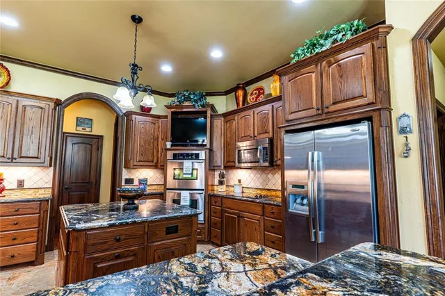 a kitchen with stainless steel appliances kitchen island granite countertop a refrigerator a stove and a sink with wooden floor